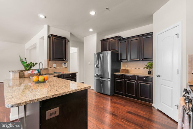 kitchen with sink, stainless steel appliances, dark hardwood / wood-style floors, light stone counters, and kitchen peninsula