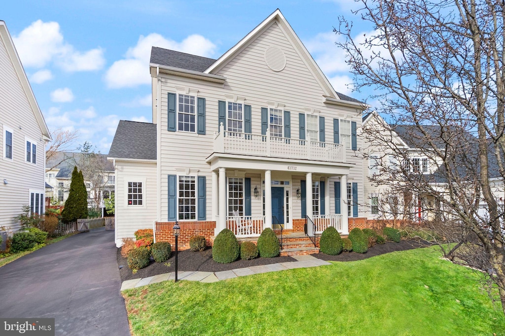 view of front of house with covered porch, a balcony, and a front lawn