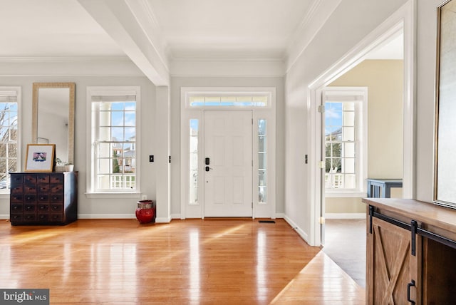 entryway featuring a wealth of natural light, ornamental molding, and light wood-type flooring