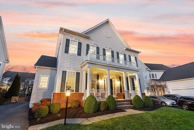 view of front facade with a porch, a balcony, and a lawn