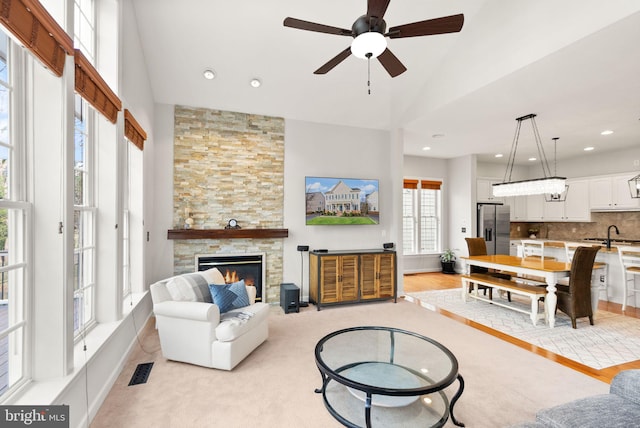 living room with a stone fireplace, ceiling fan, sink, and vaulted ceiling