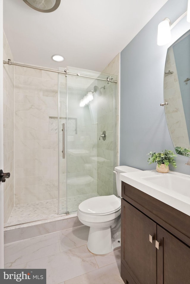 bathroom featuring a shower with door, vanity, and toilet