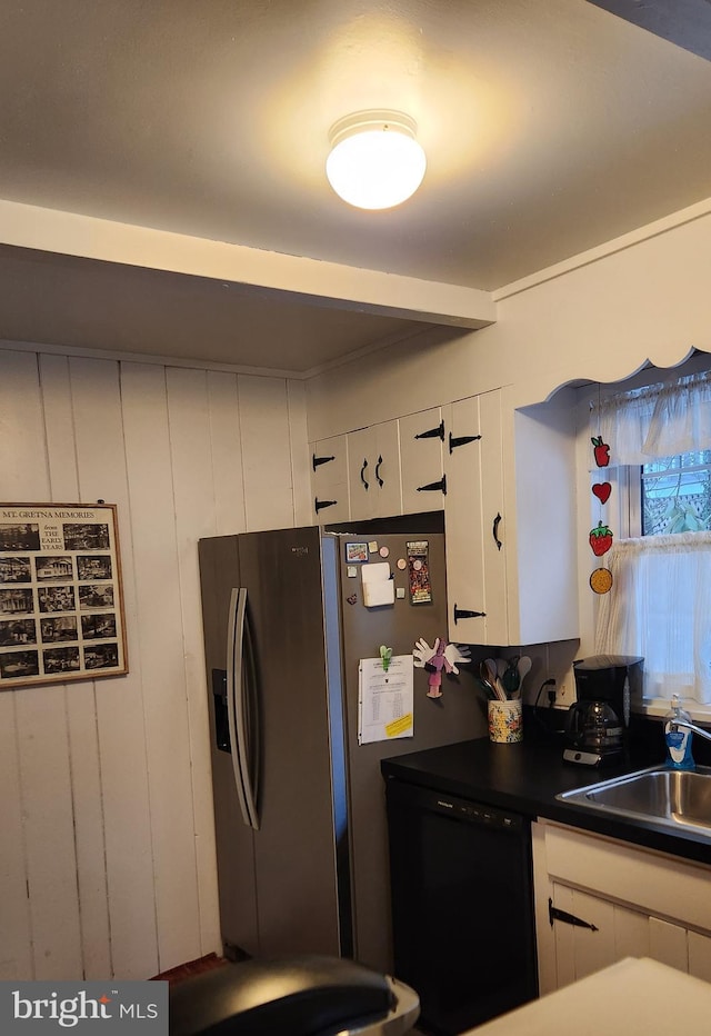 kitchen with sink, wooden walls, stainless steel fridge, black dishwasher, and white cabinetry