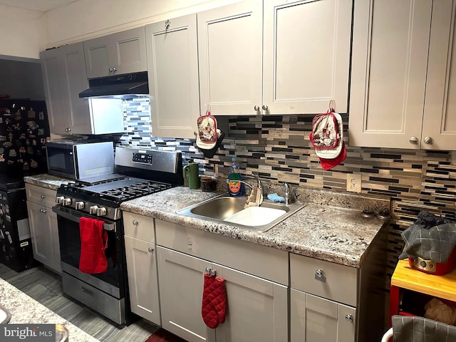 kitchen with gas range, decorative backsplash, sink, and light stone counters