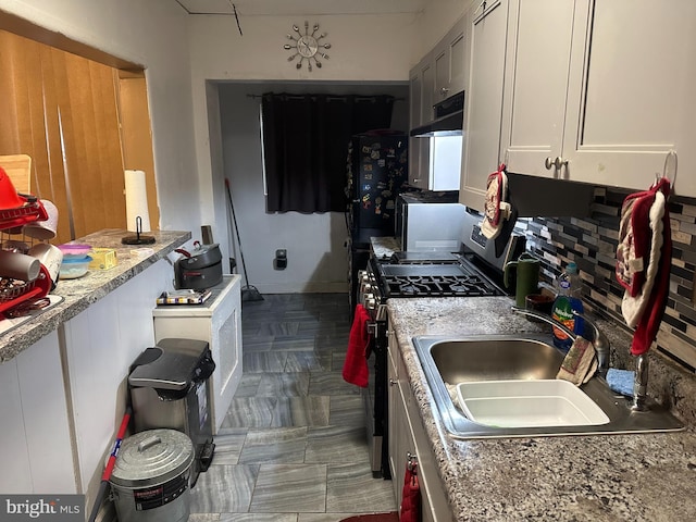 kitchen featuring white cabinets, stainless steel gas range oven, light stone counters, and sink