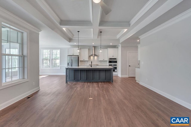 kitchen with wall chimney exhaust hood, an island with sink, appliances with stainless steel finishes, decorative light fixtures, and white cabinetry