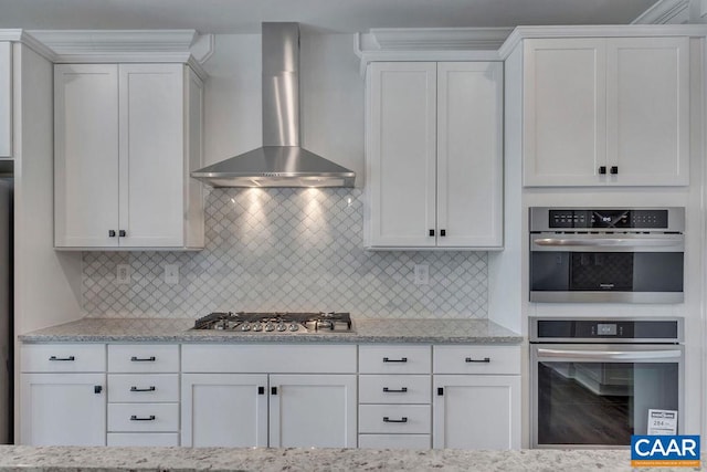 kitchen with decorative backsplash, stainless steel appliances, white cabinetry, and wall chimney range hood