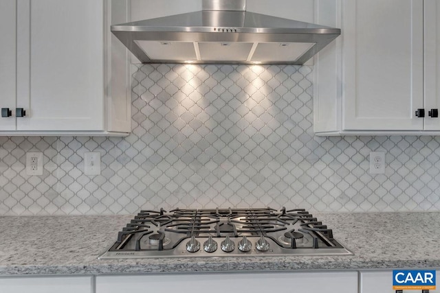 kitchen featuring decorative backsplash, light stone countertops, wall chimney exhaust hood, white cabinetry, and stainless steel gas stovetop