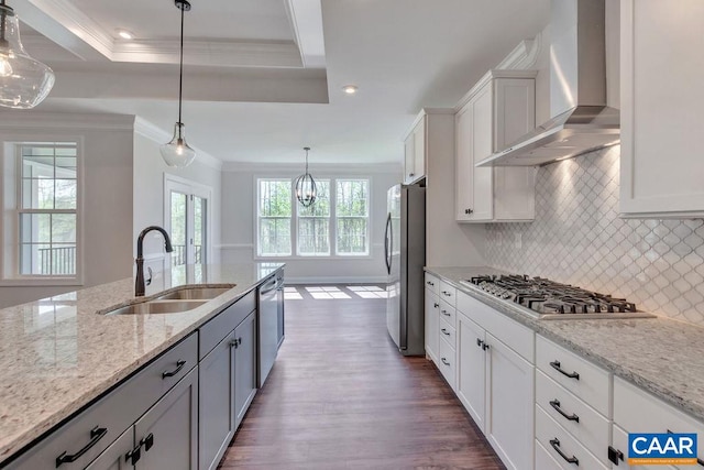 kitchen with wall chimney exhaust hood, stainless steel appliances, sink, decorative light fixtures, and white cabinets