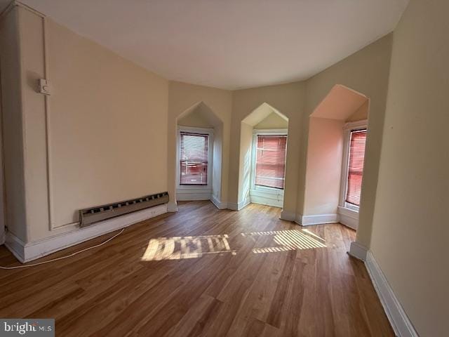 unfurnished living room featuring hardwood / wood-style flooring, baseboard heating, and a wealth of natural light