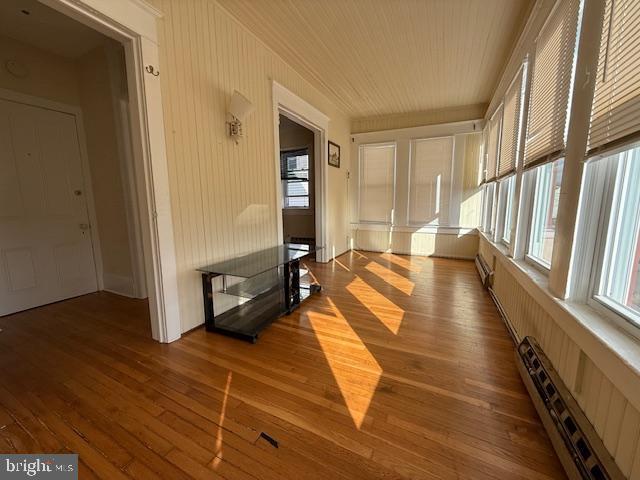 corridor featuring a healthy amount of sunlight, wood-type flooring, and baseboard heating