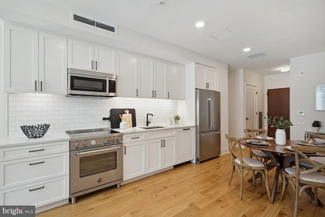 kitchen with tasteful backsplash, sink, light hardwood / wood-style flooring, high quality appliances, and white cabinets