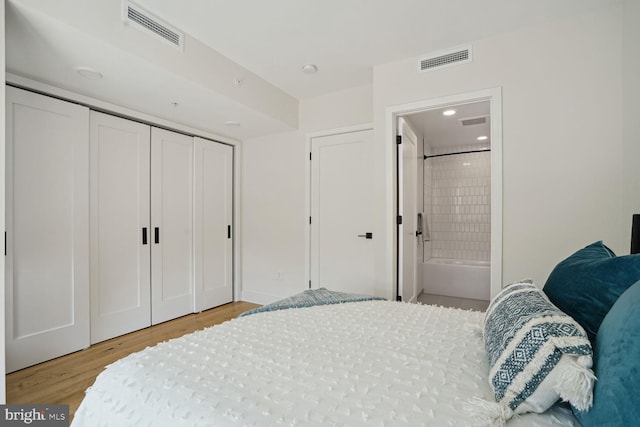 bedroom with ensuite bathroom, light wood-type flooring, and a closet