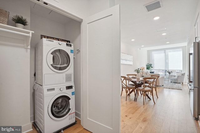 laundry area with stacked washer / drying machine and light hardwood / wood-style floors