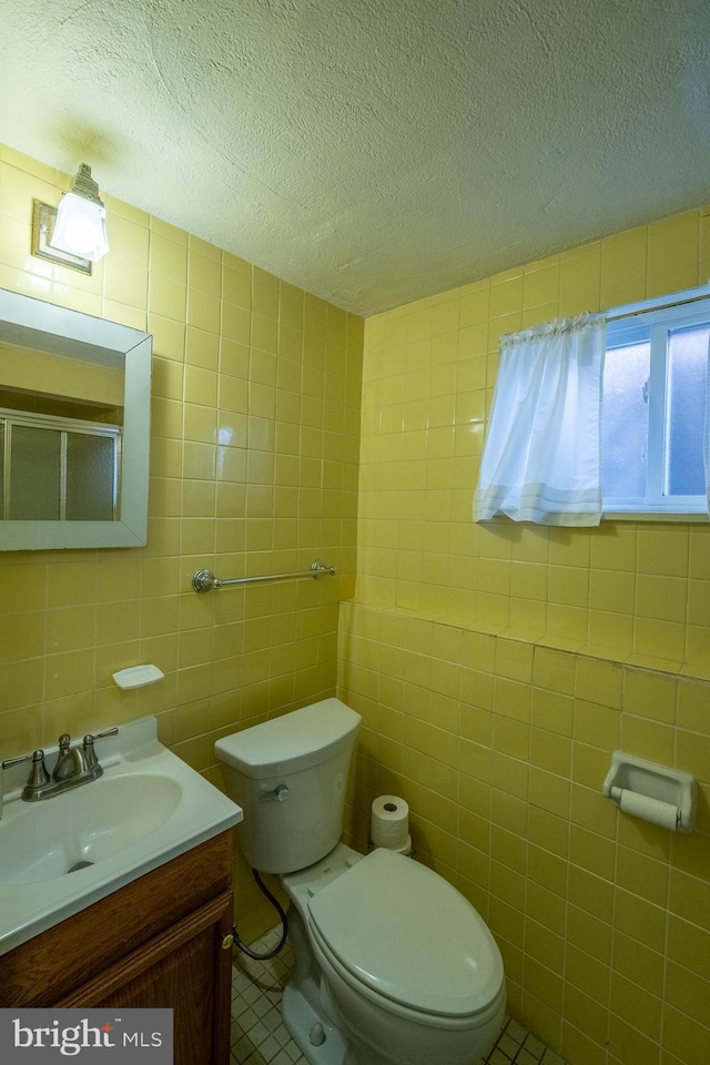 bathroom featuring tile patterned floors, a textured ceiling, vanity, tile walls, and toilet