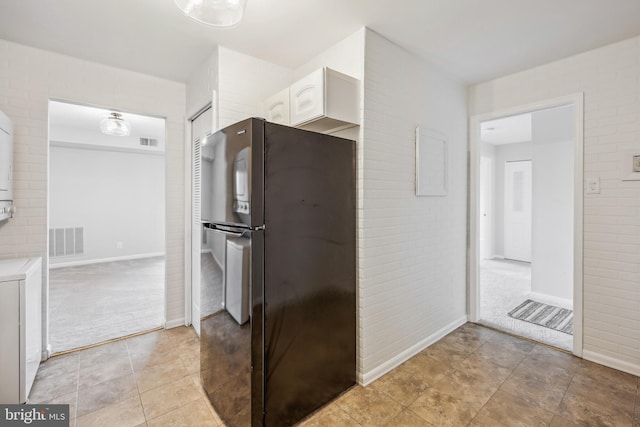 kitchen featuring stainless steel fridge, white cabinetry, light carpet, and brick wall