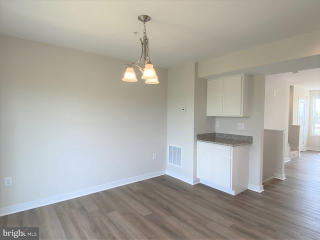 kitchen with dark stone countertops, hanging light fixtures, white cabinets, dark hardwood / wood-style flooring, and a chandelier