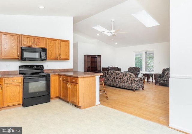 kitchen with a skylight, kitchen peninsula, ceiling fan, light hardwood / wood-style floors, and black appliances