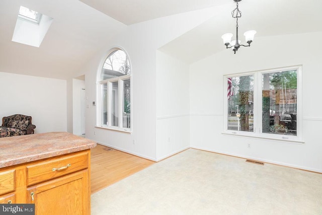 dining area with lofted ceiling with skylight, a chandelier, and light hardwood / wood-style floors