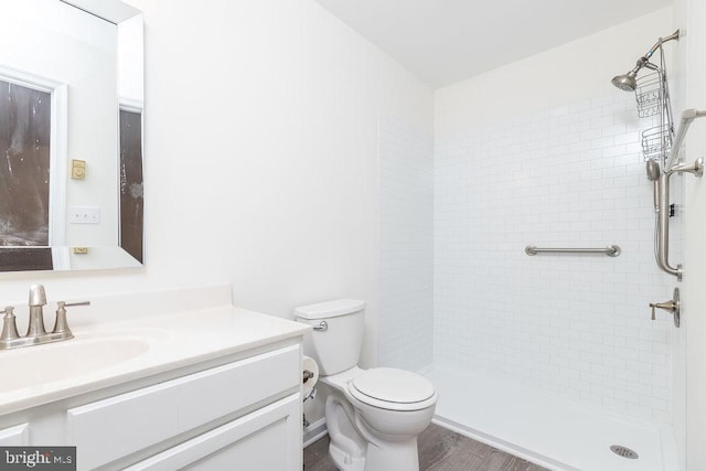 bathroom featuring vanity, wood-type flooring, tiled shower, and toilet