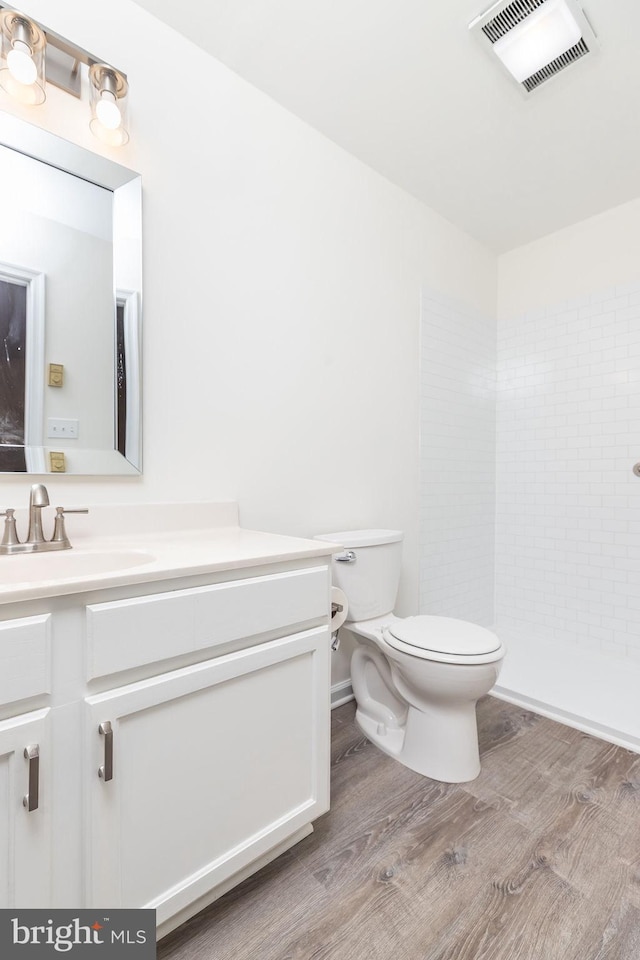 bathroom featuring wood-type flooring, tiled shower, vanity, and toilet