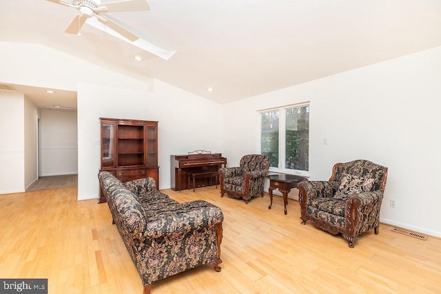 living area with ceiling fan, vaulted ceiling with skylight, and light wood-type flooring