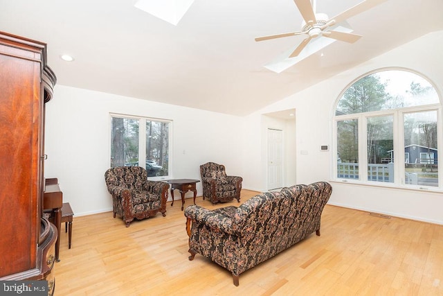 living room with ceiling fan, vaulted ceiling with skylight, and light wood-type flooring