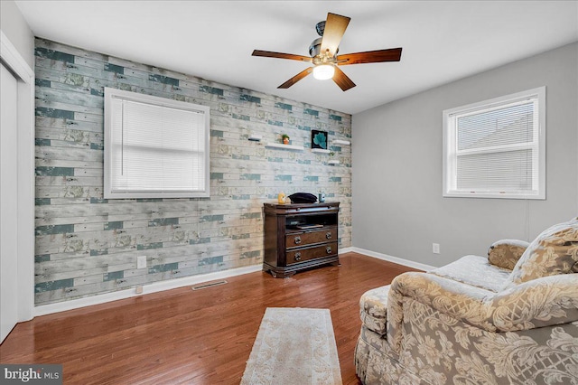 living area with dark hardwood / wood-style flooring, ceiling fan, and wooden walls