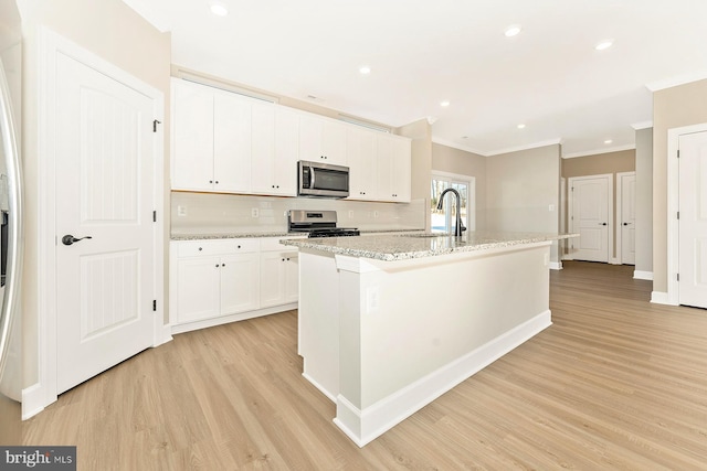 kitchen with white cabinets, appliances with stainless steel finishes, an island with sink, light hardwood / wood-style floors, and sink