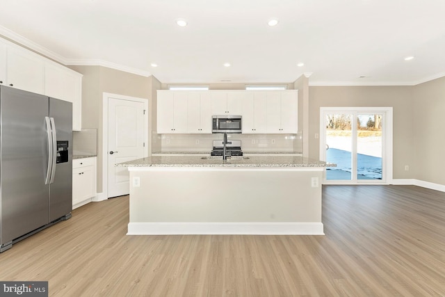 kitchen featuring white cabinetry, light wood-type flooring, stainless steel appliances, light stone counters, and a center island with sink