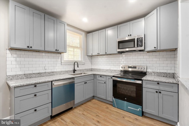 kitchen with sink, stainless steel appliances, gray cabinets, decorative backsplash, and light wood-type flooring