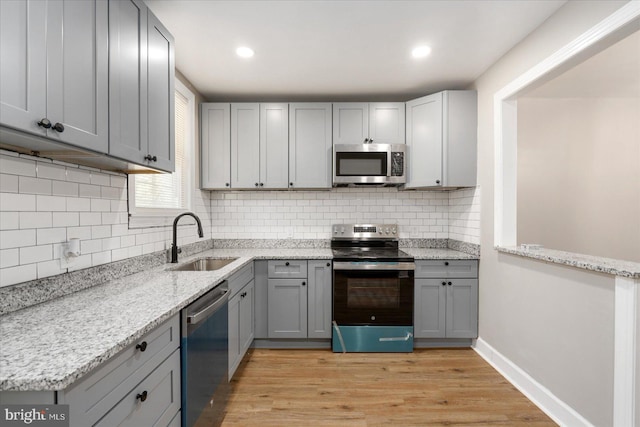 kitchen with appliances with stainless steel finishes, light hardwood / wood-style floors, gray cabinetry, and sink