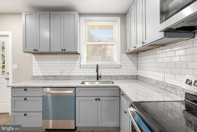 kitchen with light stone countertops, appliances with stainless steel finishes, gray cabinetry, and sink