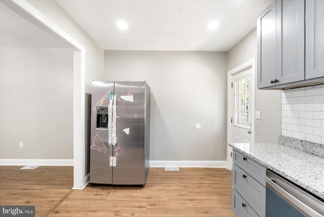 kitchen featuring stainless steel appliances, light stone counters, gray cabinets, decorative backsplash, and light wood-type flooring