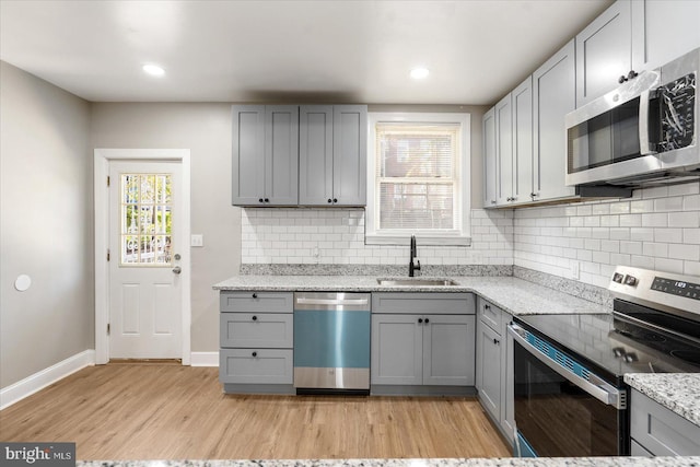 kitchen with stainless steel appliances, light stone counters, gray cabinetry, and sink