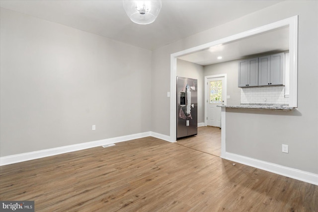 interior space with light hardwood / wood-style flooring, gray cabinets, light stone countertops, tasteful backsplash, and stainless steel fridge with ice dispenser