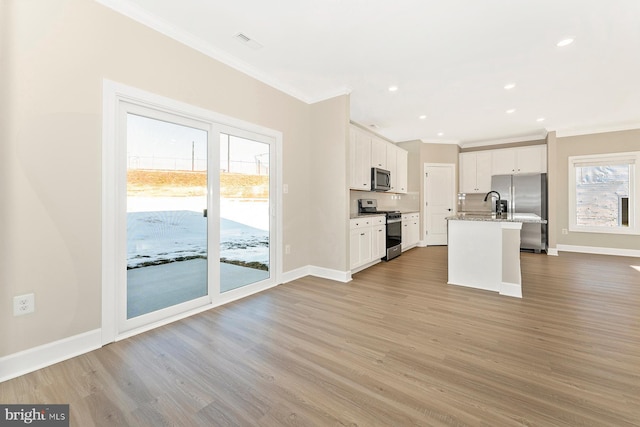 kitchen featuring appliances with stainless steel finishes, white cabinetry, ornamental molding, a kitchen island with sink, and light wood-type flooring