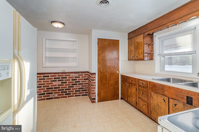 kitchen with brick wall, white refrigerator with ice dispenser, sink, built in features, and stove