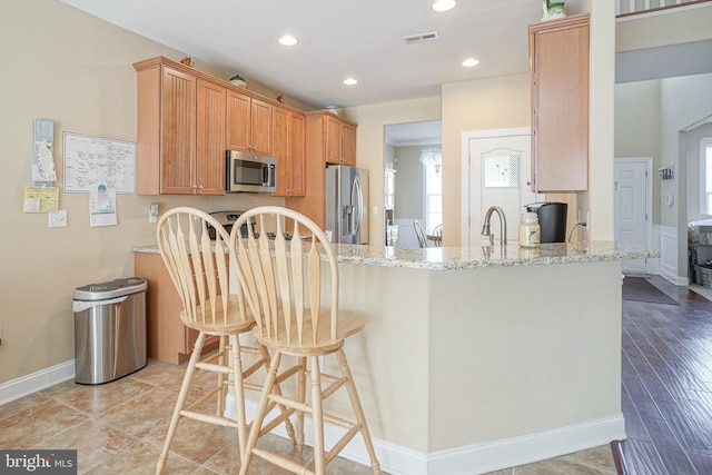 kitchen with visible vents, a peninsula, light stone countertops, stainless steel appliances, and recessed lighting