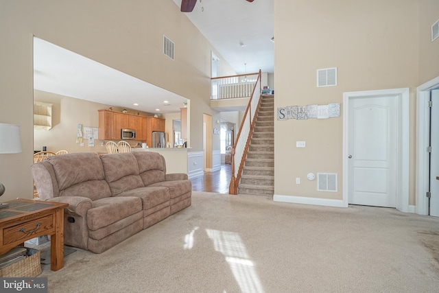 living area featuring stairs, visible vents, and light colored carpet