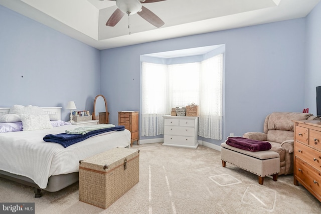 bedroom featuring a ceiling fan, a tray ceiling, light colored carpet, and baseboards