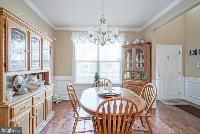 dining space featuring a decorative wall, a wainscoted wall, a notable chandelier, wood finished floors, and ornamental molding