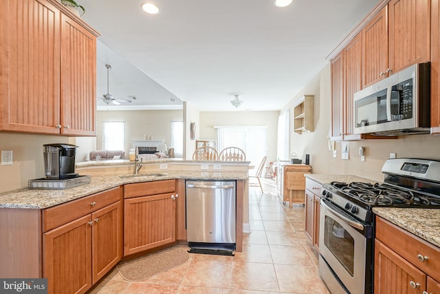 kitchen with light tile patterned floors, appliances with stainless steel finishes, open floor plan, a sink, and light stone countertops