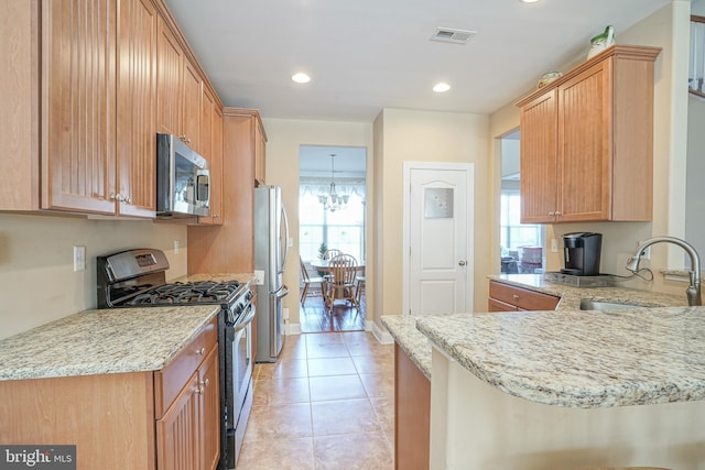 kitchen with visible vents, light stone counters, a peninsula, stainless steel appliances, and a sink