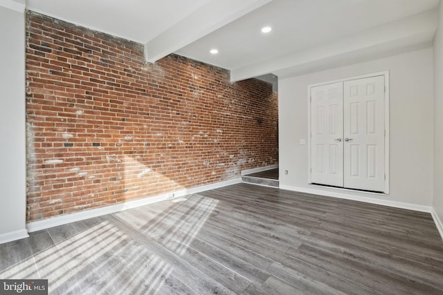 empty room featuring beamed ceiling, dark wood-type flooring, and brick wall