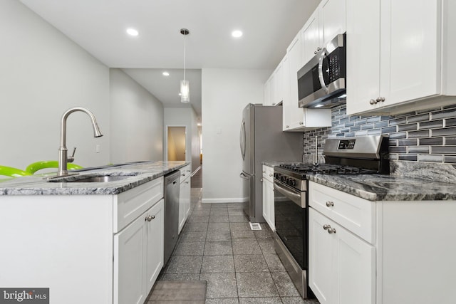 kitchen with sink, dark stone countertops, appliances with stainless steel finishes, decorative light fixtures, and white cabinetry