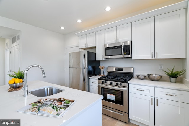 kitchen with sink, stainless steel appliances, light stone counters, light hardwood / wood-style flooring, and white cabinets