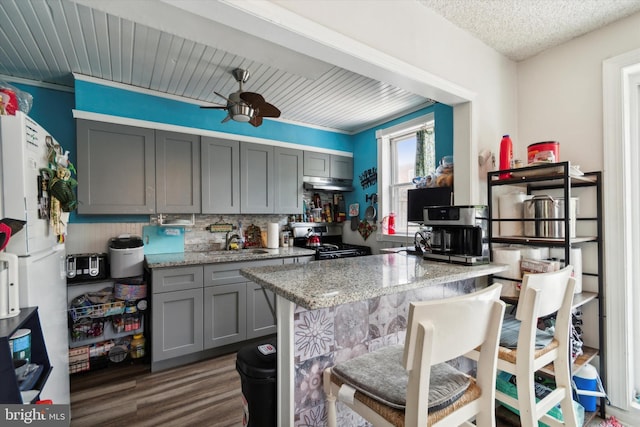 kitchen with gas stove, gray cabinetry, light stone countertops, and white refrigerator