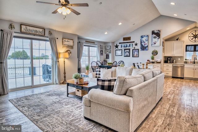 living room with ceiling fan, light hardwood / wood-style floors, and vaulted ceiling