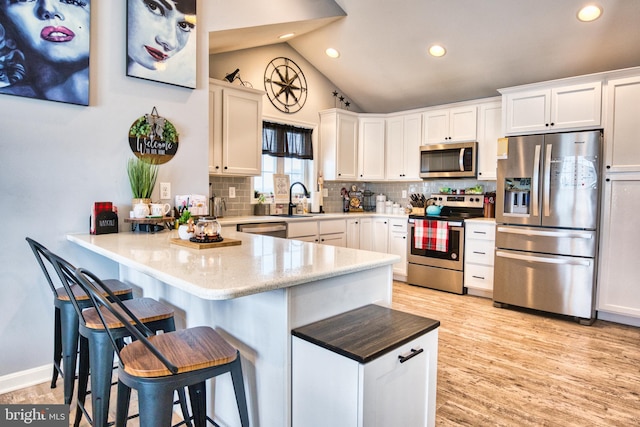 kitchen featuring a kitchen bar, appliances with stainless steel finishes, kitchen peninsula, sink, and white cabinets